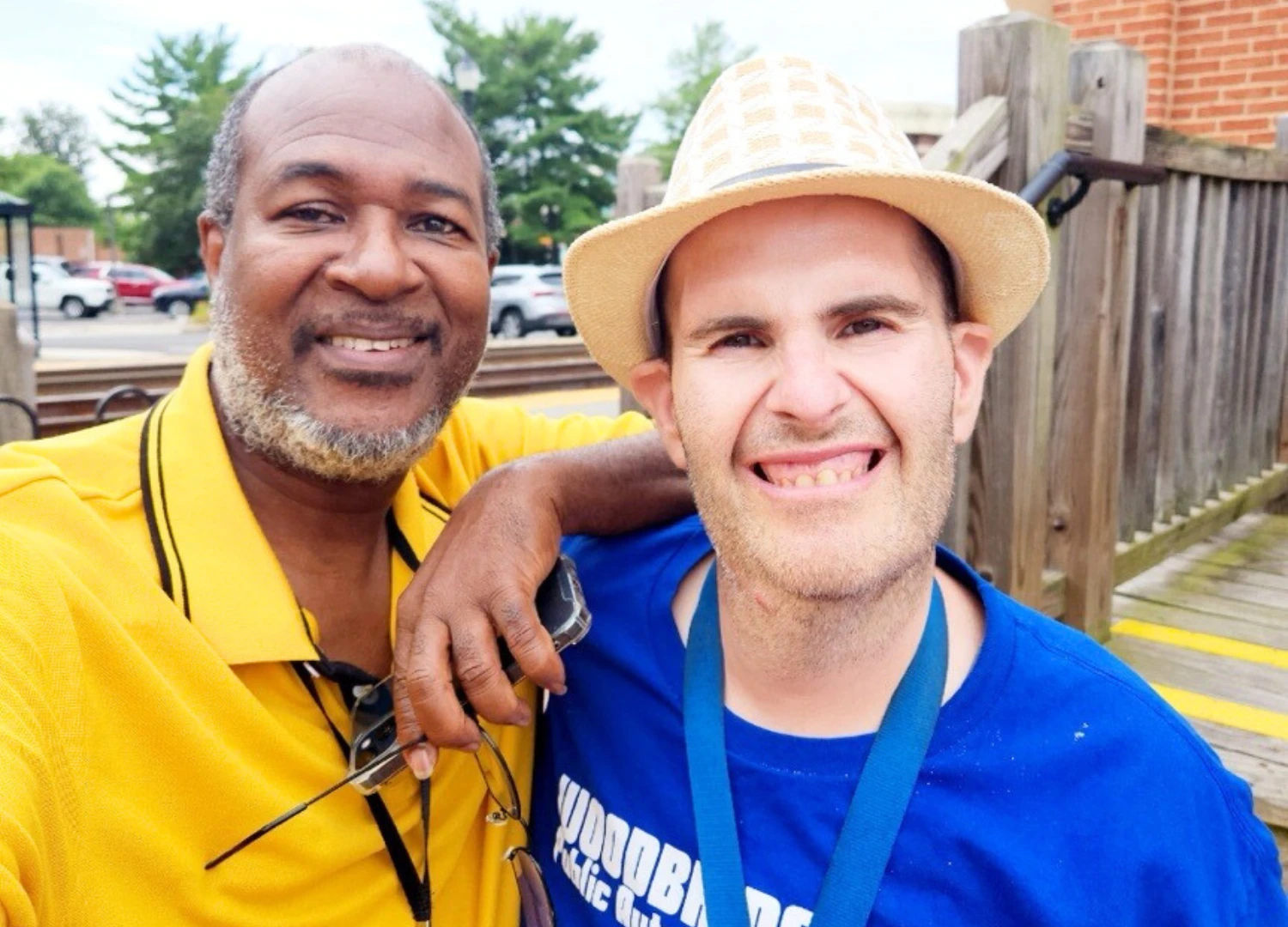 PrivateServicesBanner What appears to be two men taking a selfie outdoors; one in a yellow polo, the other in a blue shirt and straw hat, arms around each other by a wooden fence.
