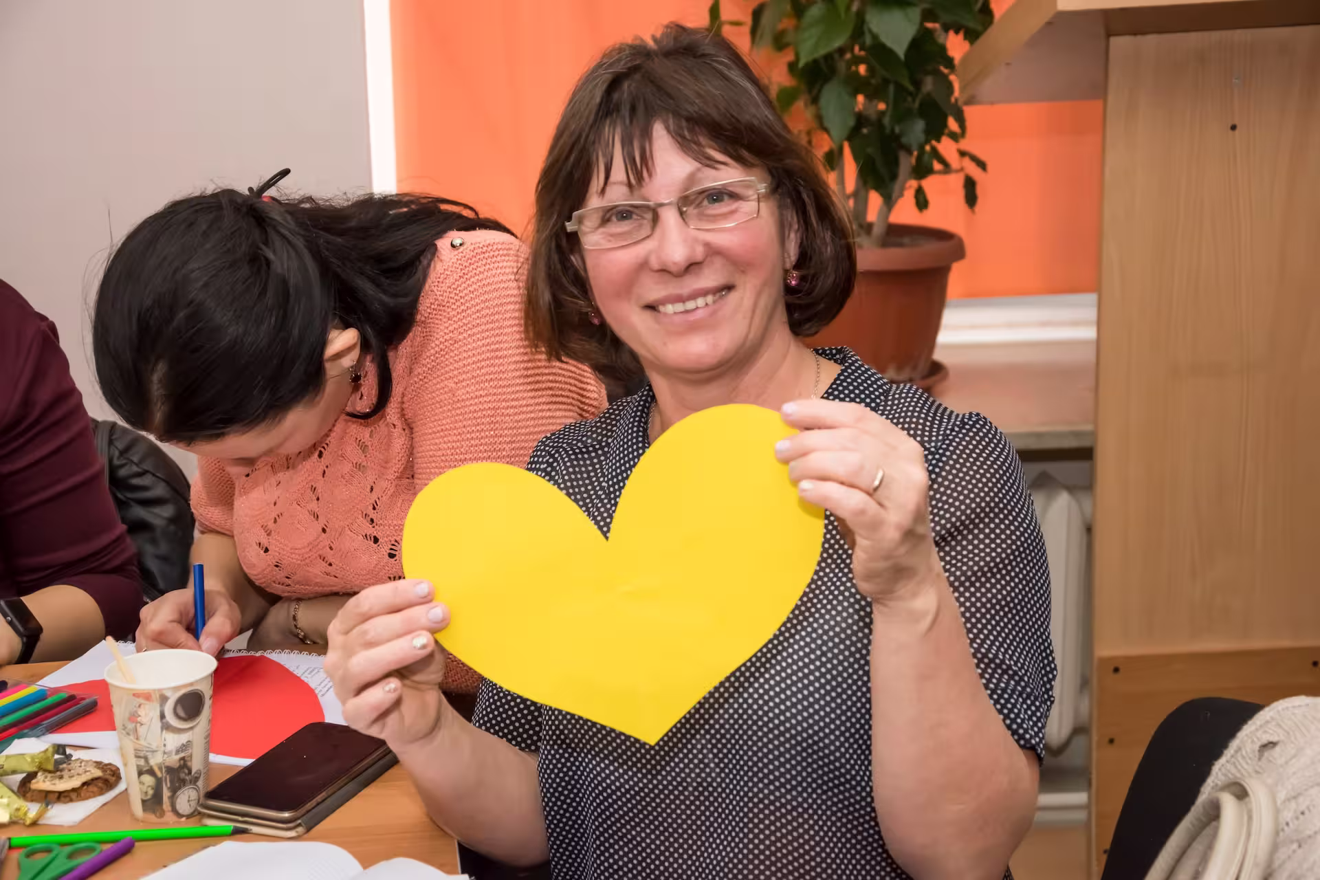 Person smiling and holding a yellow, crafted heart